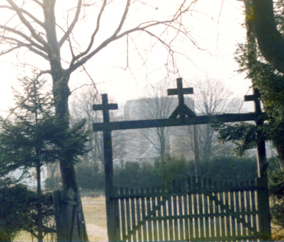 Röm. kath. Friedhof: Eingangsbereich mit Holztor, auf dessen oberem Querbalken drei Kreuzen aufgesetzt sind